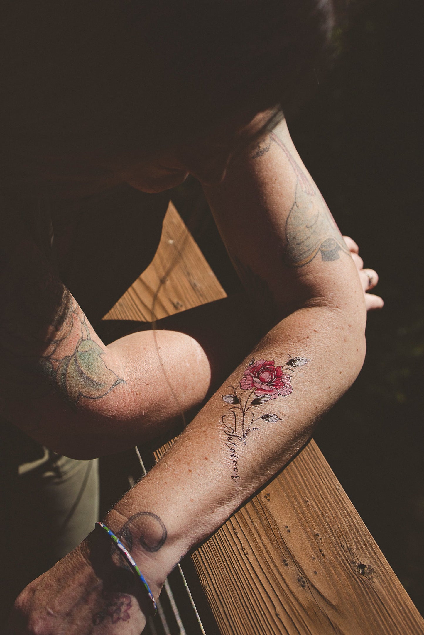 Small red peony flower tattoo on forearm with stem and leaves