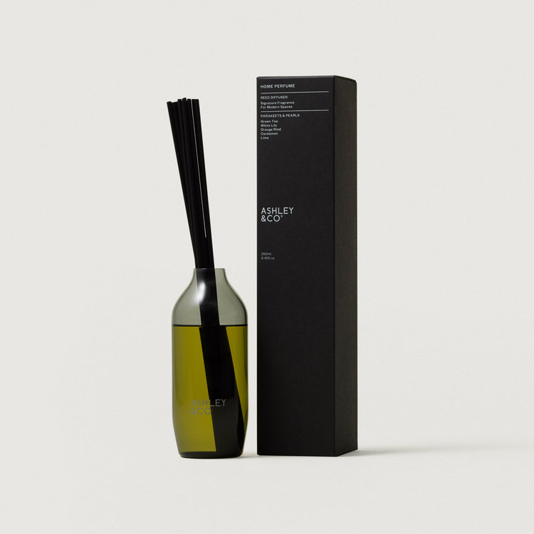 Reed diffuser bottle with upright black reeds next to rectangular black gift box