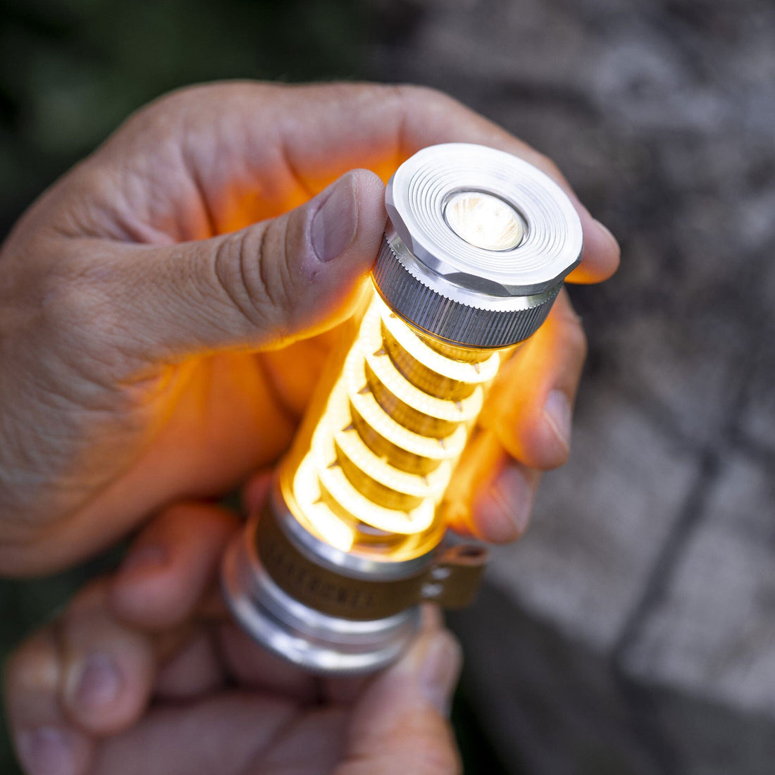 Handheld silver Edison light stick showing warm LEDs through ribbed housing