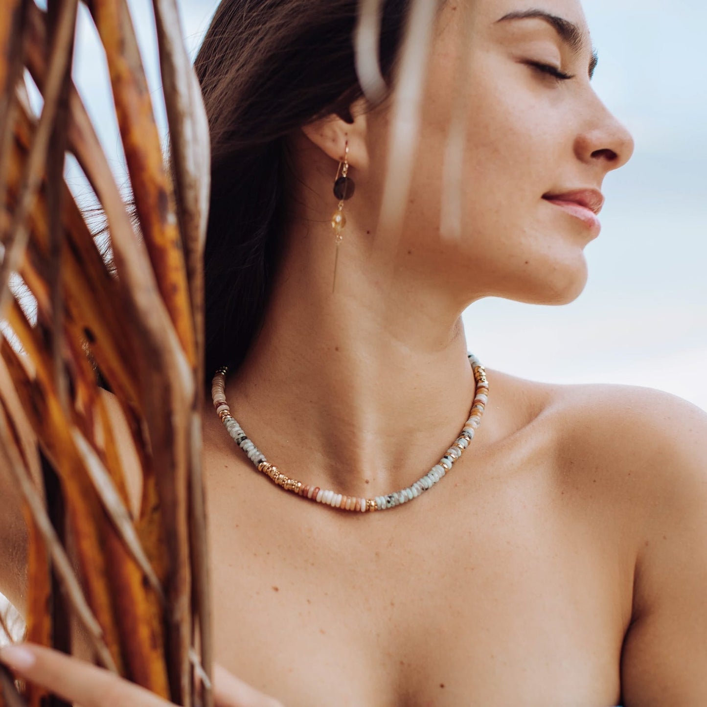 Beaded gold-tone necklace resting at collarbone with light blue/gray and gold beads