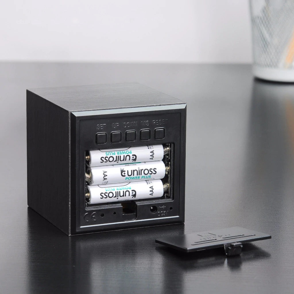 Black cube digital clock with blue LED, open battery compartment and buttons