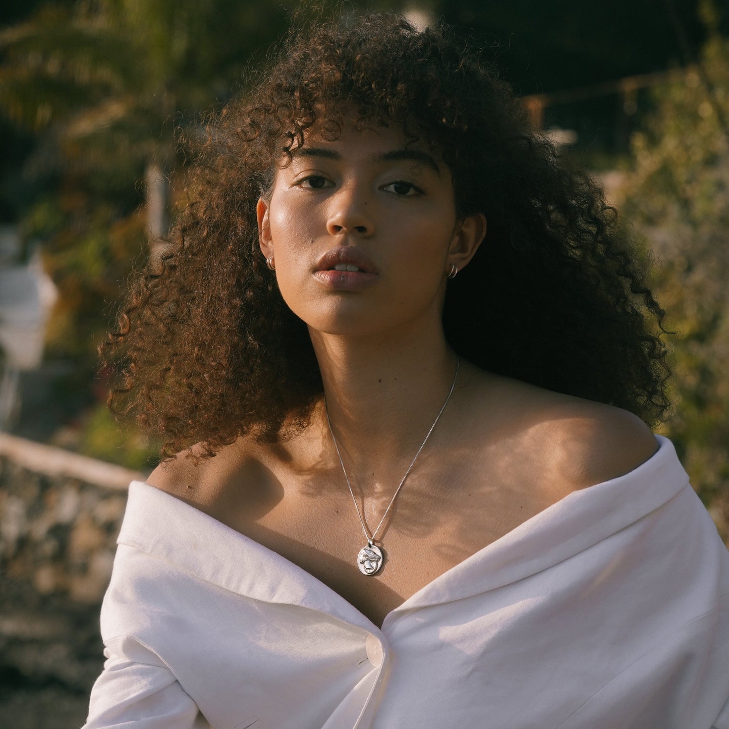 Silver circular pendant necklace with thin chain, visible at the neckline