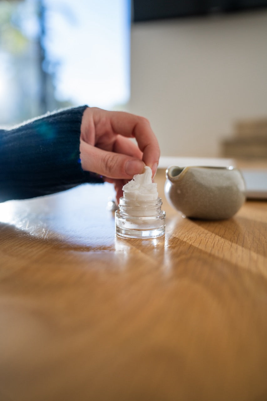 Aromatherapy eye cover set ingredient: spoon pouring oil blend beside glass jar