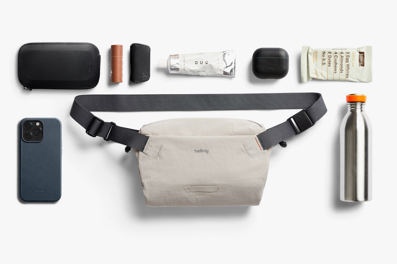 Mini sling bag flat lay with essentials, including phone, bottle, and black pouch.