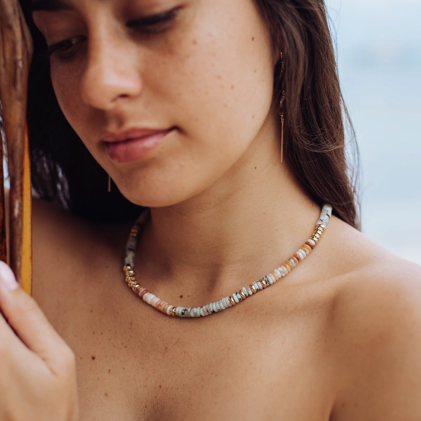Beaded gold-tone necklace detail with light blue/gray beads and gold accents on neck