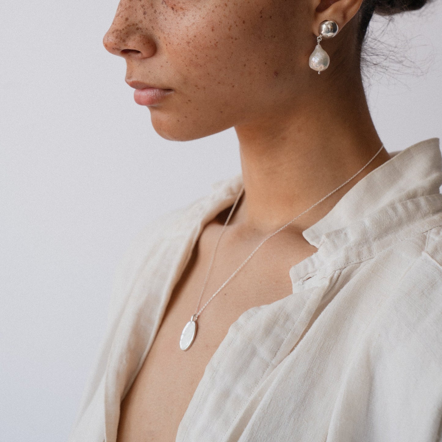 Silver oval pendant necklace on delicate chain, worn close-up