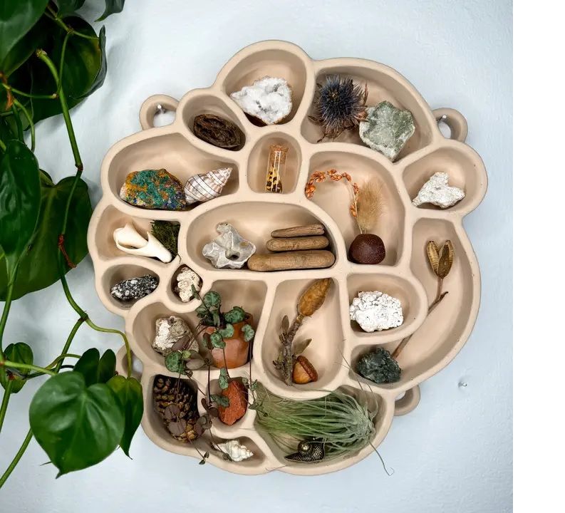 Beige round cement inspiration shelf with curved compartments and small decorative objects inside.