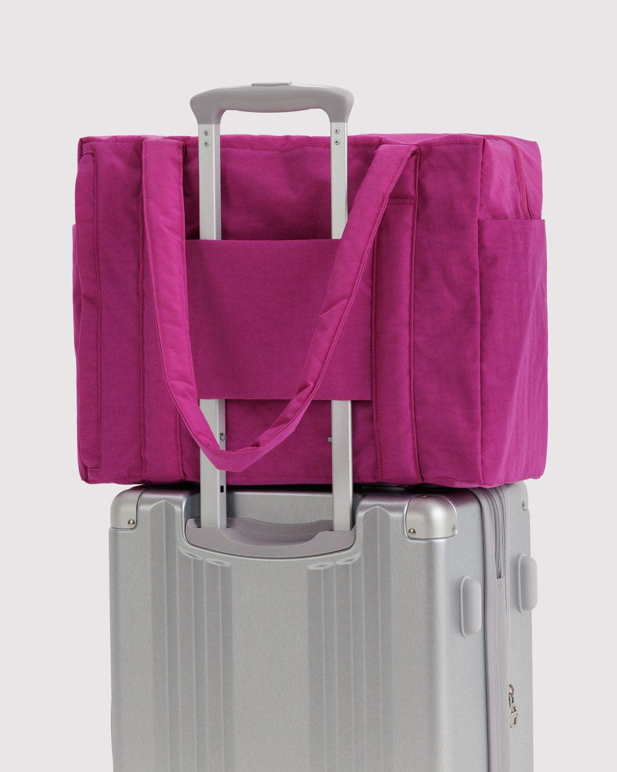 Pink carry-on tote bag attached to a rolling suitcase with a handle pass-through