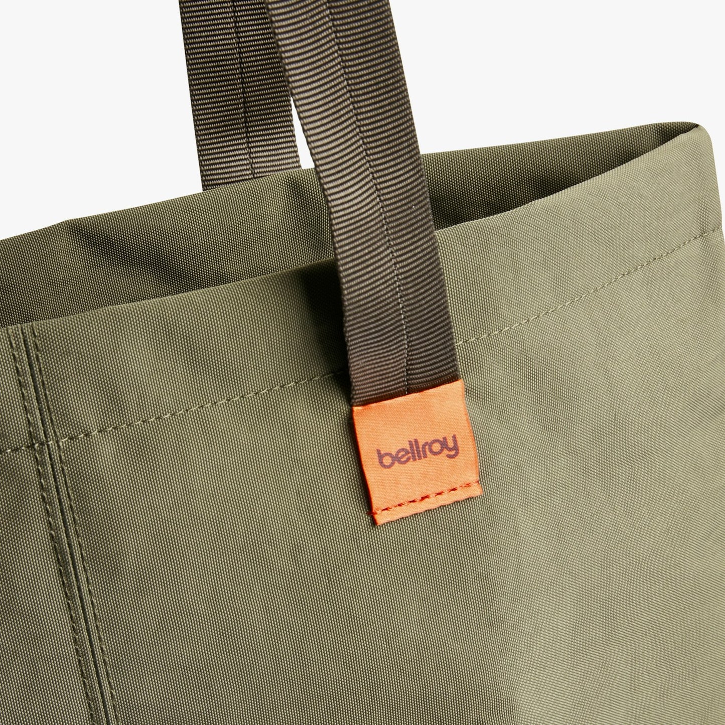 City tote bag strap close-up with visible stitching and an orange brand label patch.