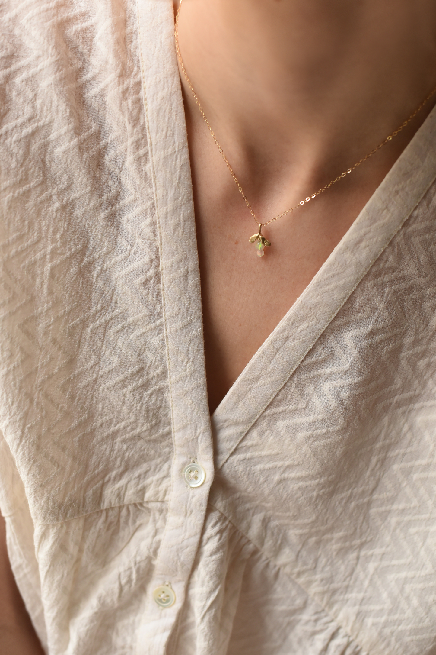 Gold leaf drop necklace with small green opal pendant resting on the neckline