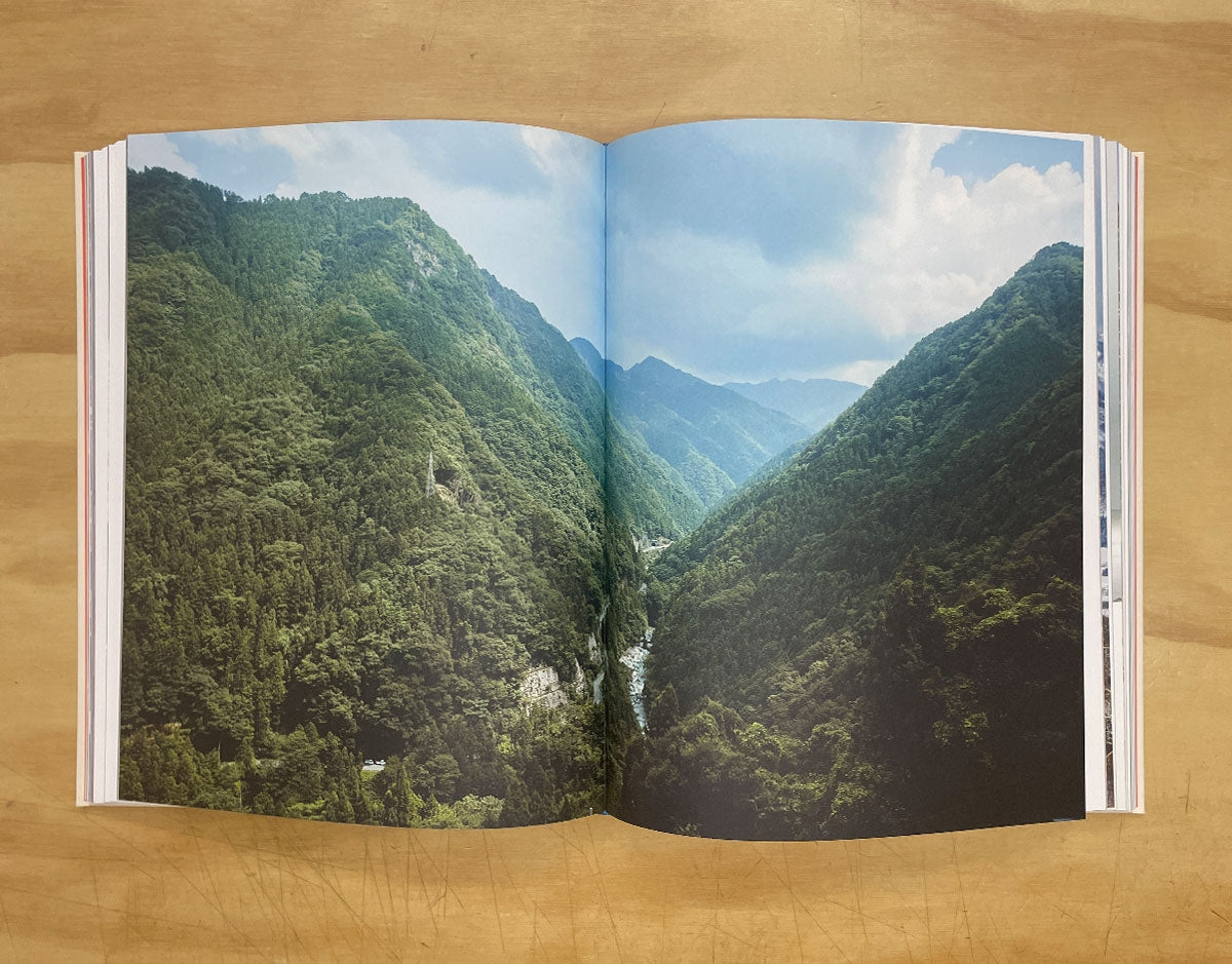 Open hardcover book spread with panoramic mountain landscape and valley river