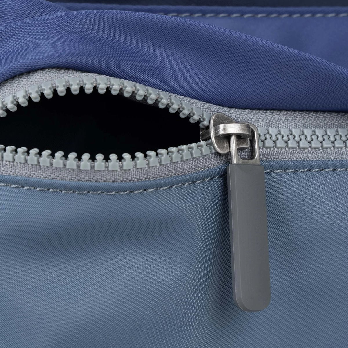 Light blue nylon crossbody bag with gray zipper pull and stitched zipper track