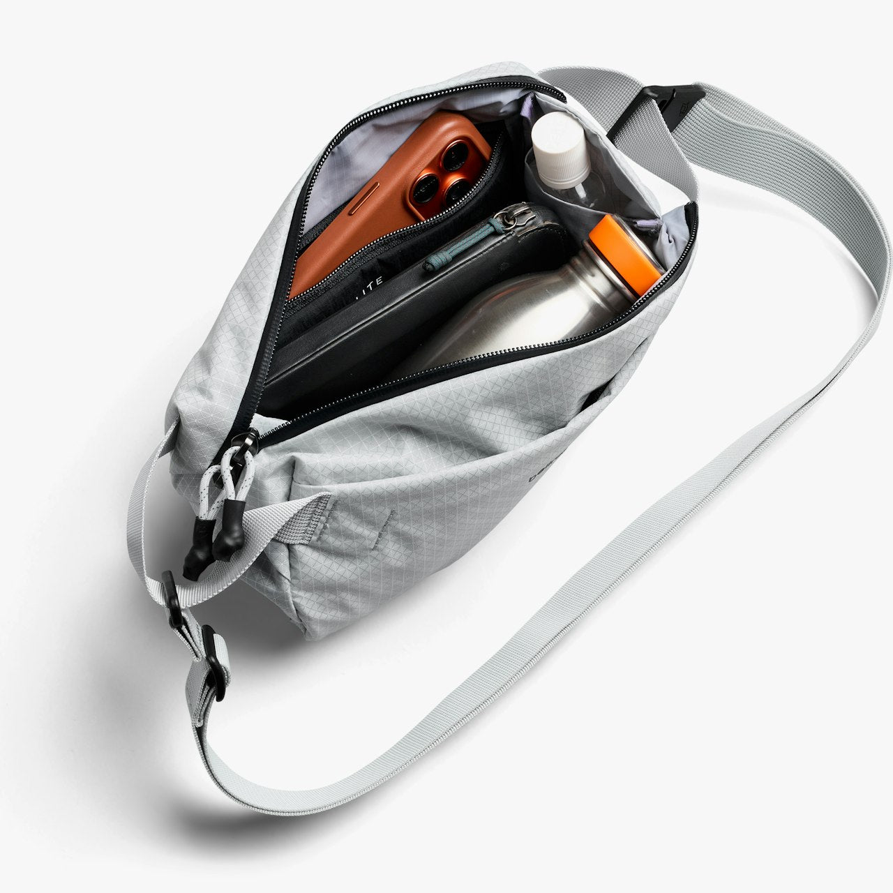 Light gray mini sling bag opened, with water bottle, orange case, and small accessories.