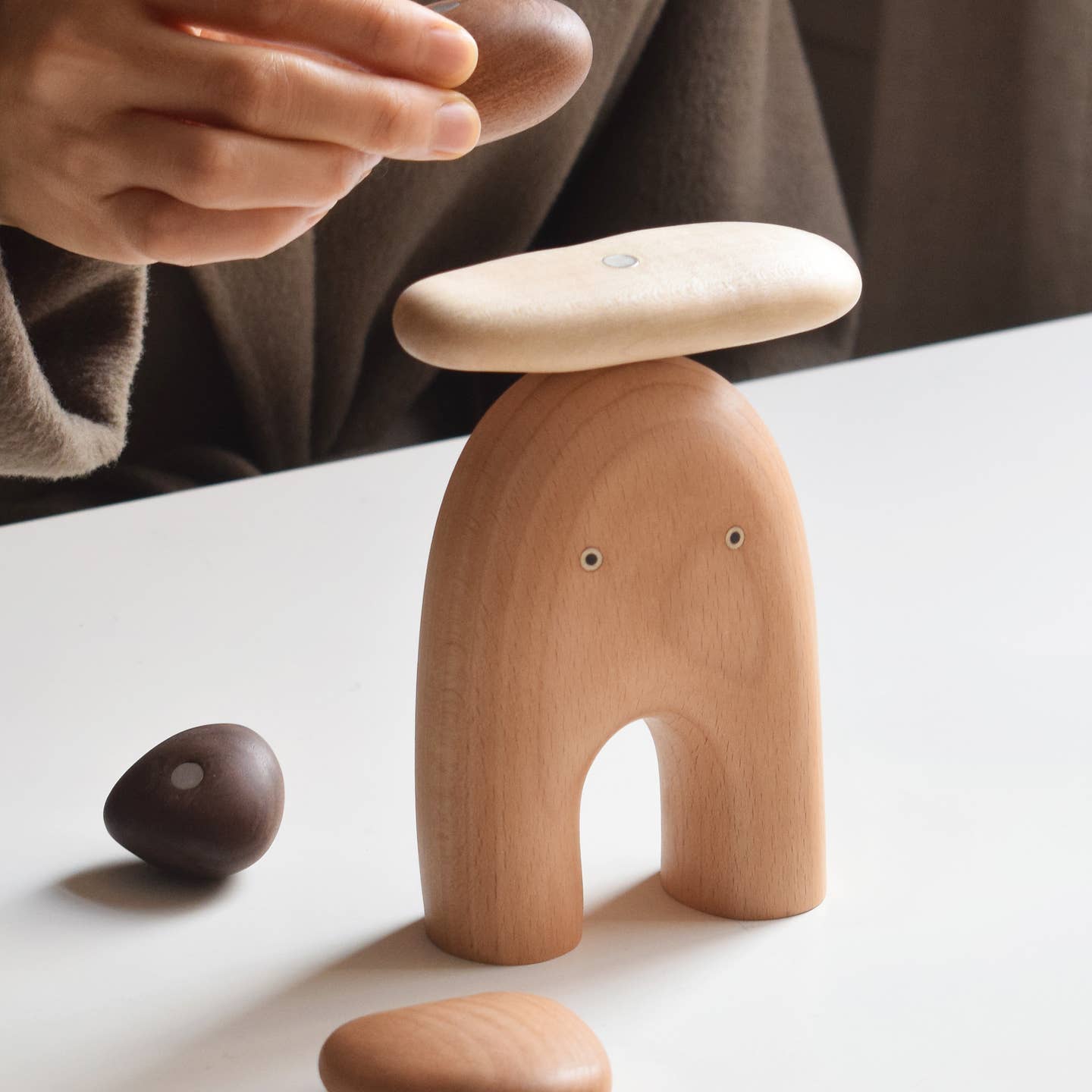 Wooden elf balancing stones figure on table, close-up with round stones and hand