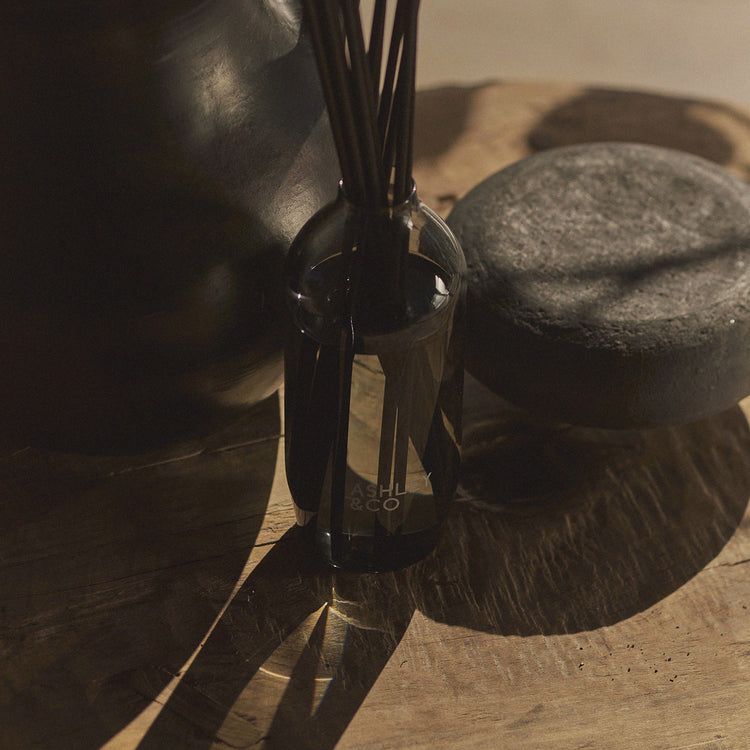 Reed diffuser bottle with black reeds in glass on stone tabletop