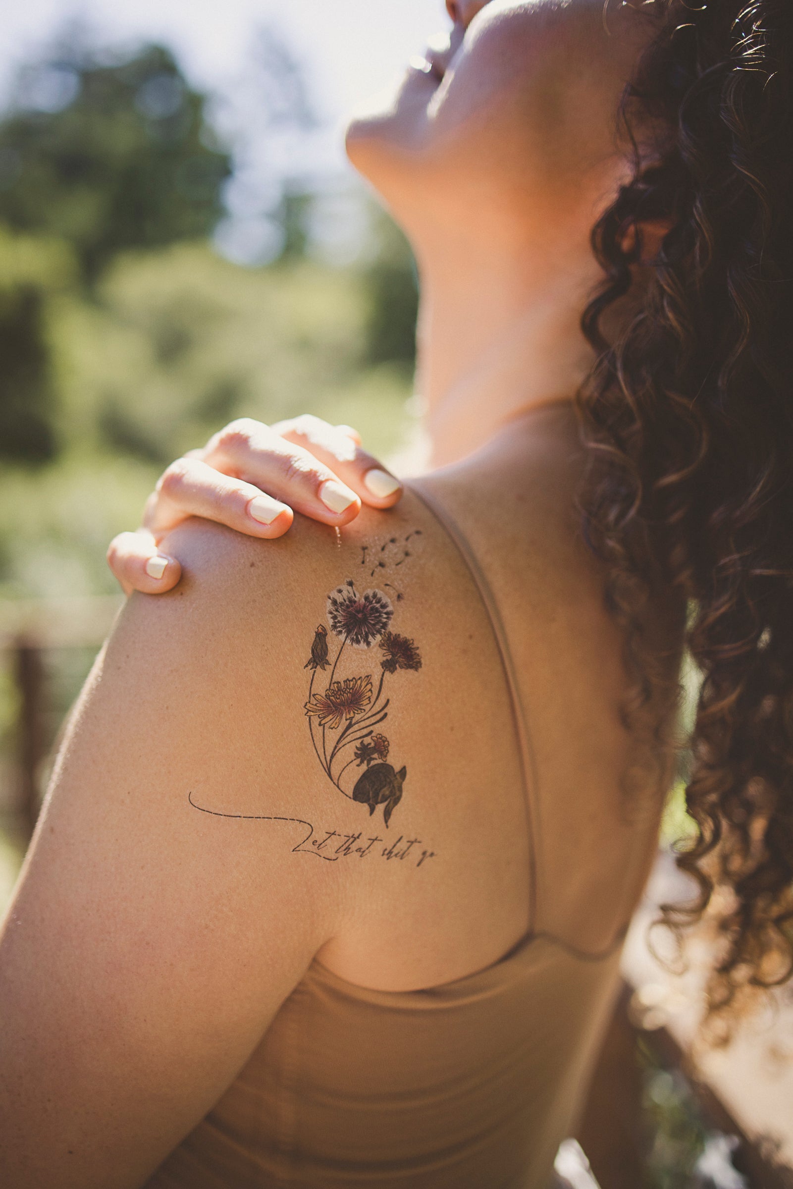Small floral intention tattoo on upper chest/shoulder with dandelion and script.