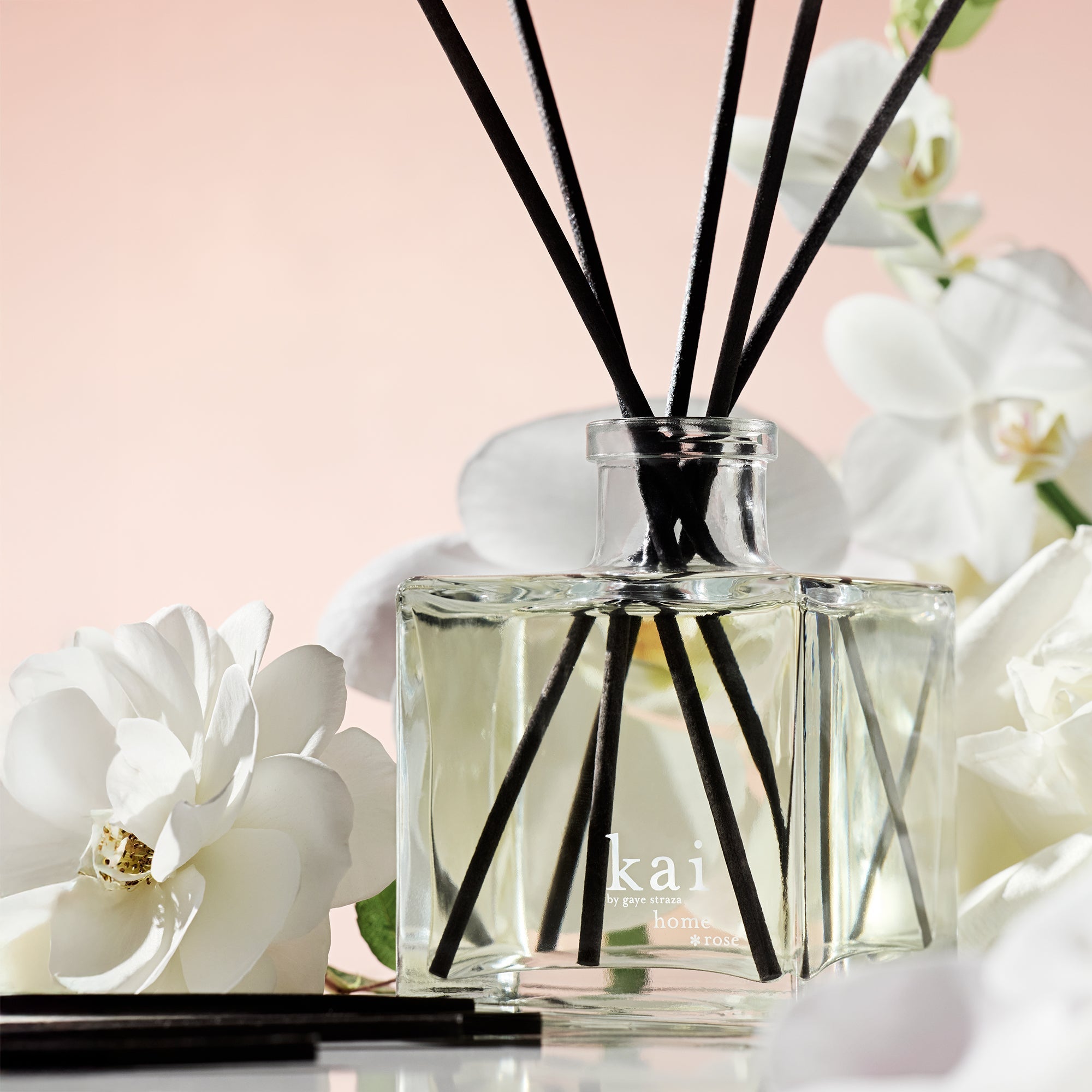 Glass reed diffuser bottle with black reeds, clear bottle near white flowers