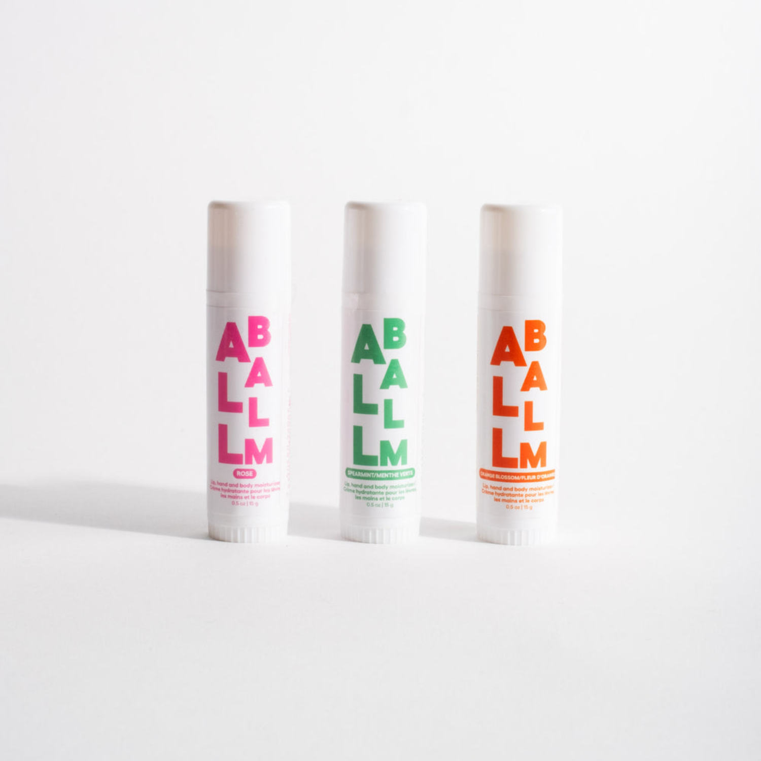 All balm stick set of three scents with pink, green, and orange labels in white tubes.
