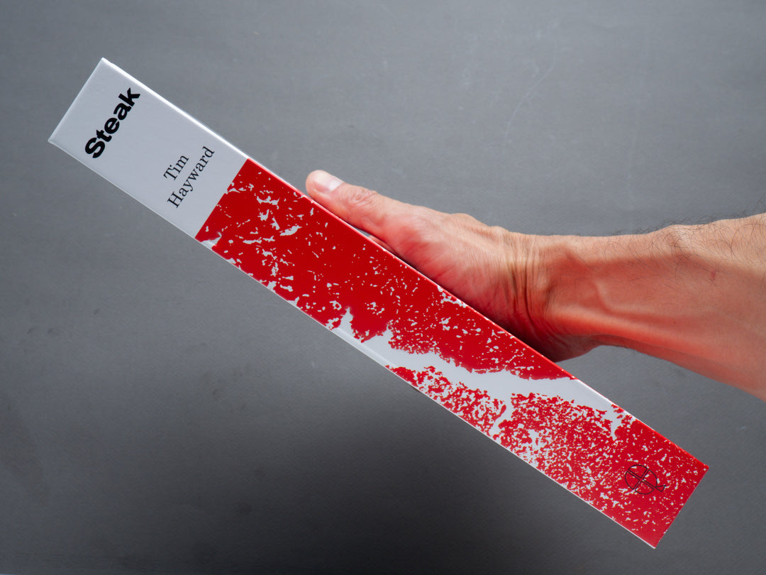Hand holding a red speckled book cover with angled bold title and author name