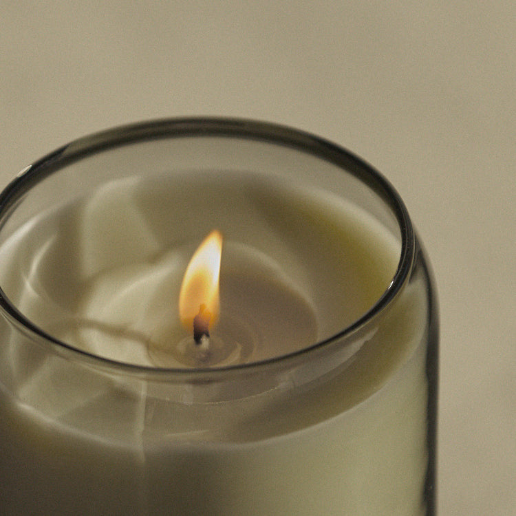 Close-up of lit flame inside smoky olive glass waxed perfume candle