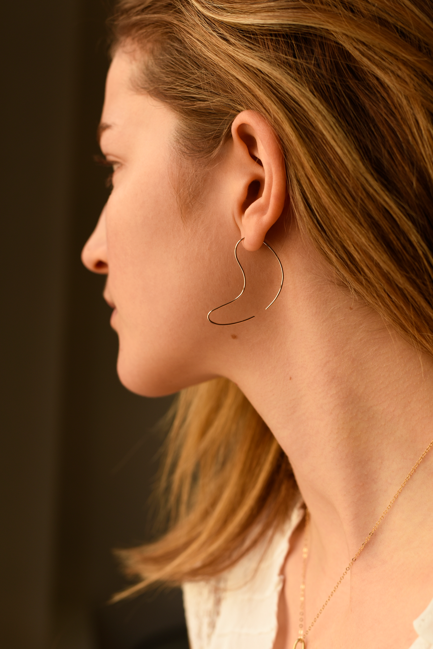 Large sculpted curve hoop threader earrings, thin gold-tone wire, side profile view