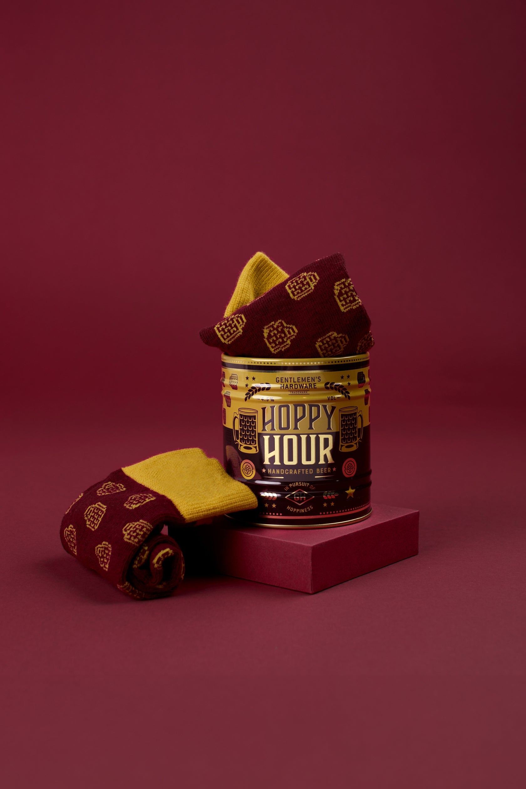 Folded beer-themed socks with gold pattern beside Hoppy Hour sock can