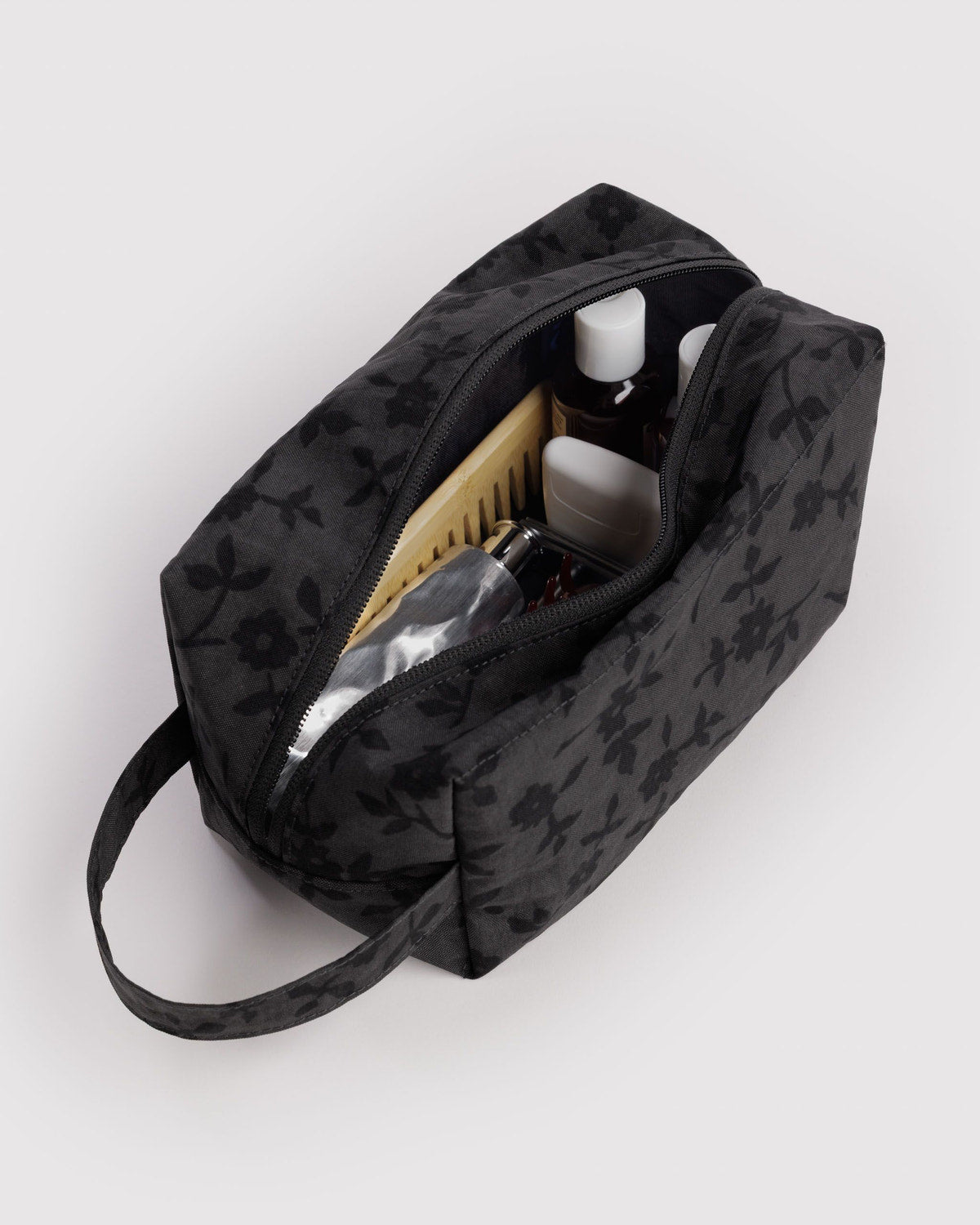 Black floral dopp kit with open zipper and toiletry bottles inside