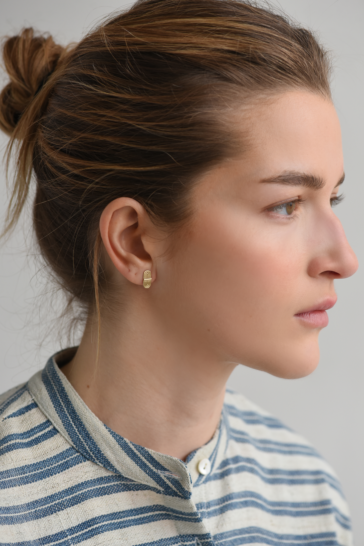 Gold-tone double-arc stud earrings on side view, curved bar front