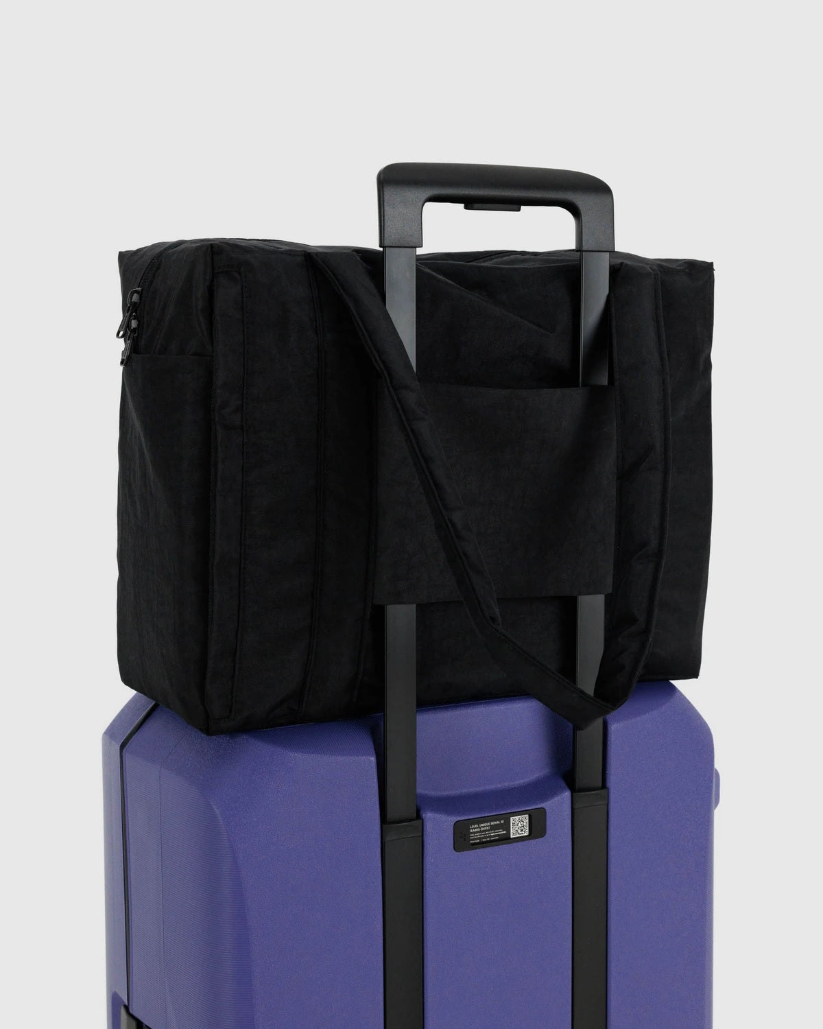 Small Cloud carry-on with black tote cover over purple hard-shell base and front pocket