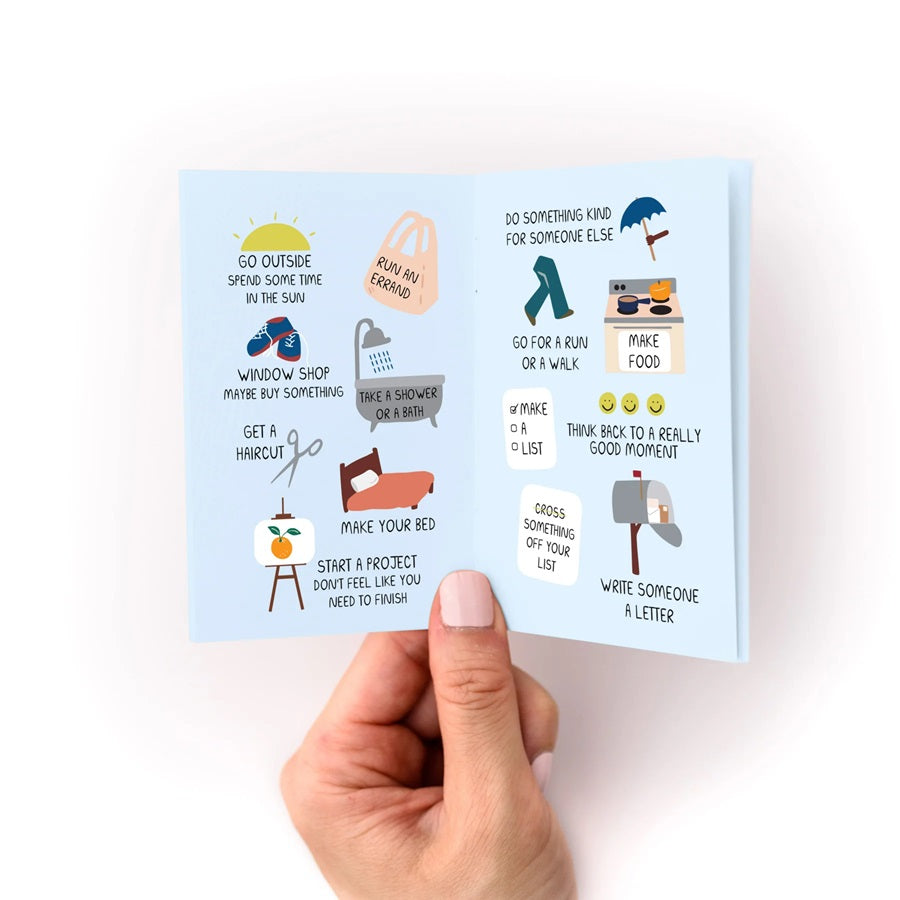 Open zine with teal pages featuring illustrated self-care prompts and short text lines
