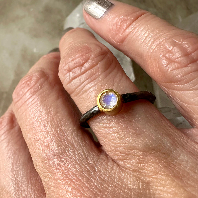 Moonstone ring on finger with oxidized dark silver band and gold bezel blue stone