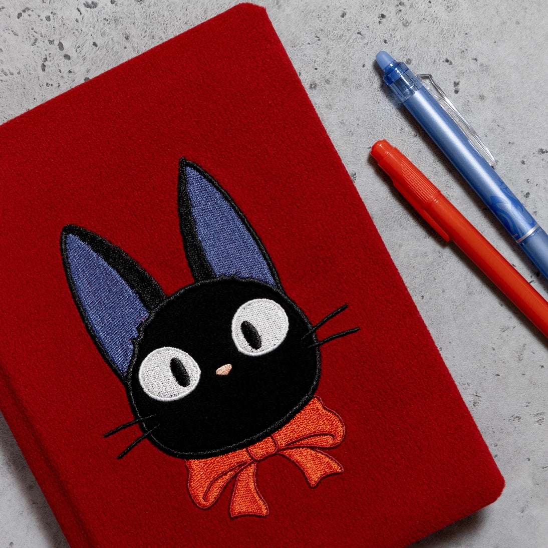 Red plush journal cover with large Jiji black cat face and orange bow