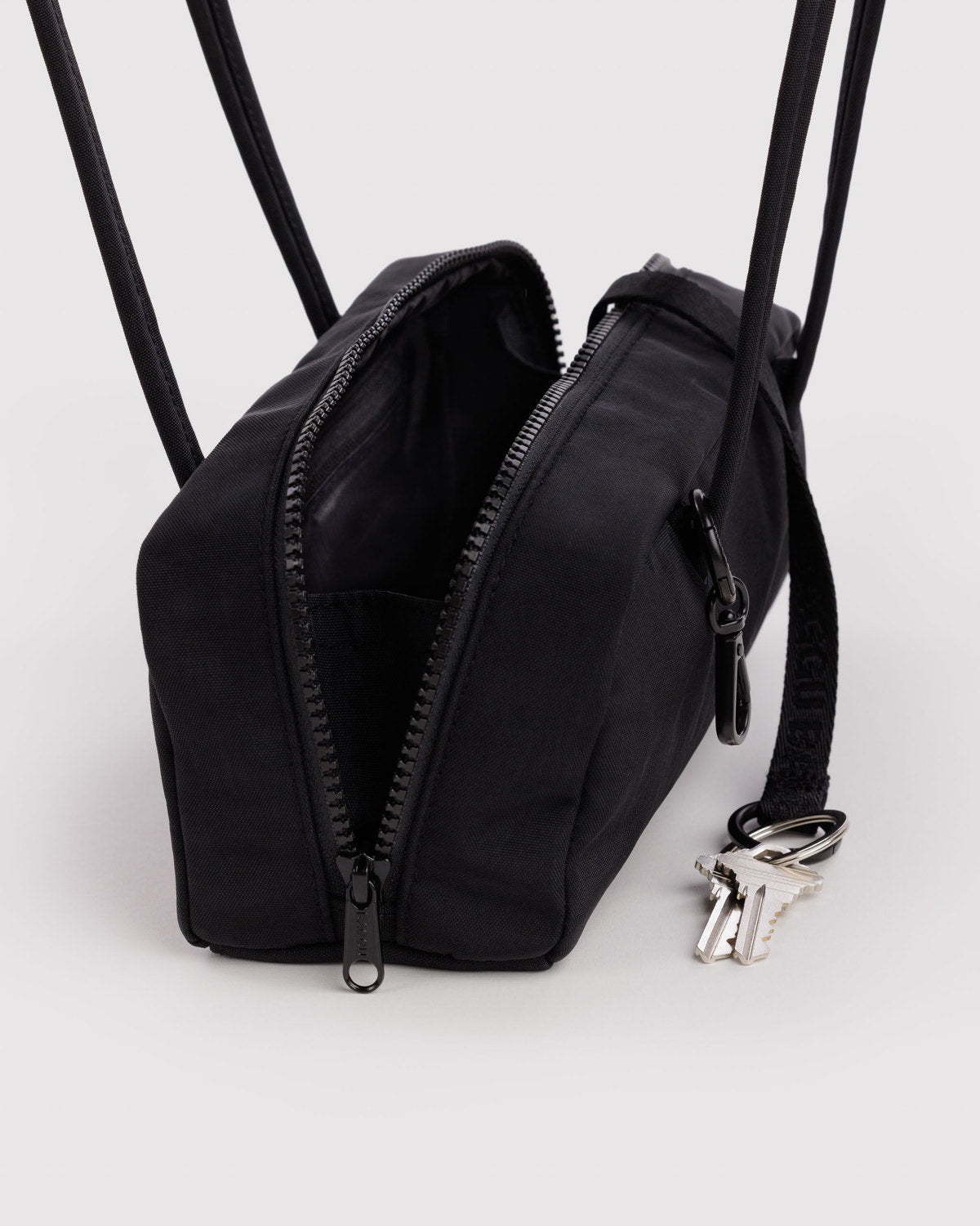 Small nylon bowler bag in black, front zipper detail and long straps.