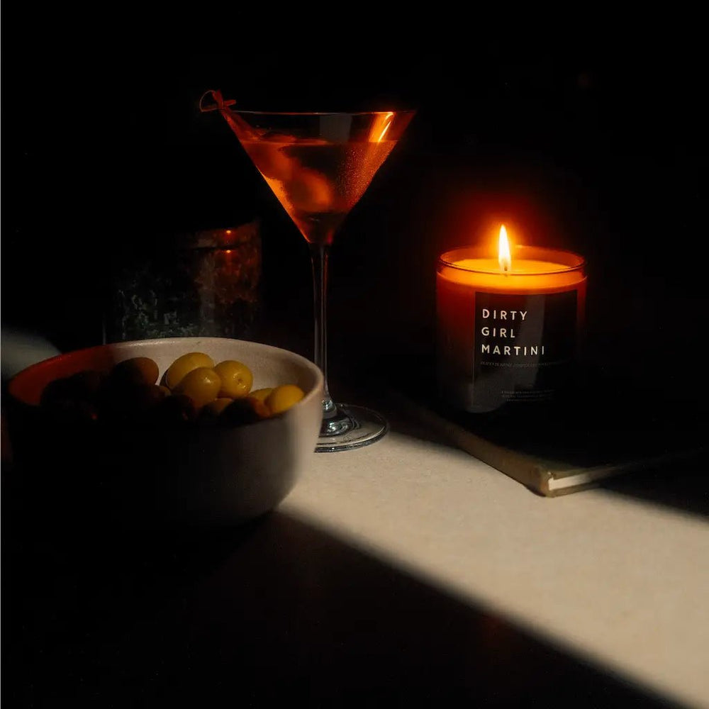 Lit Dirty Girl Martini soy wax candle in dark glass jar with visible wick