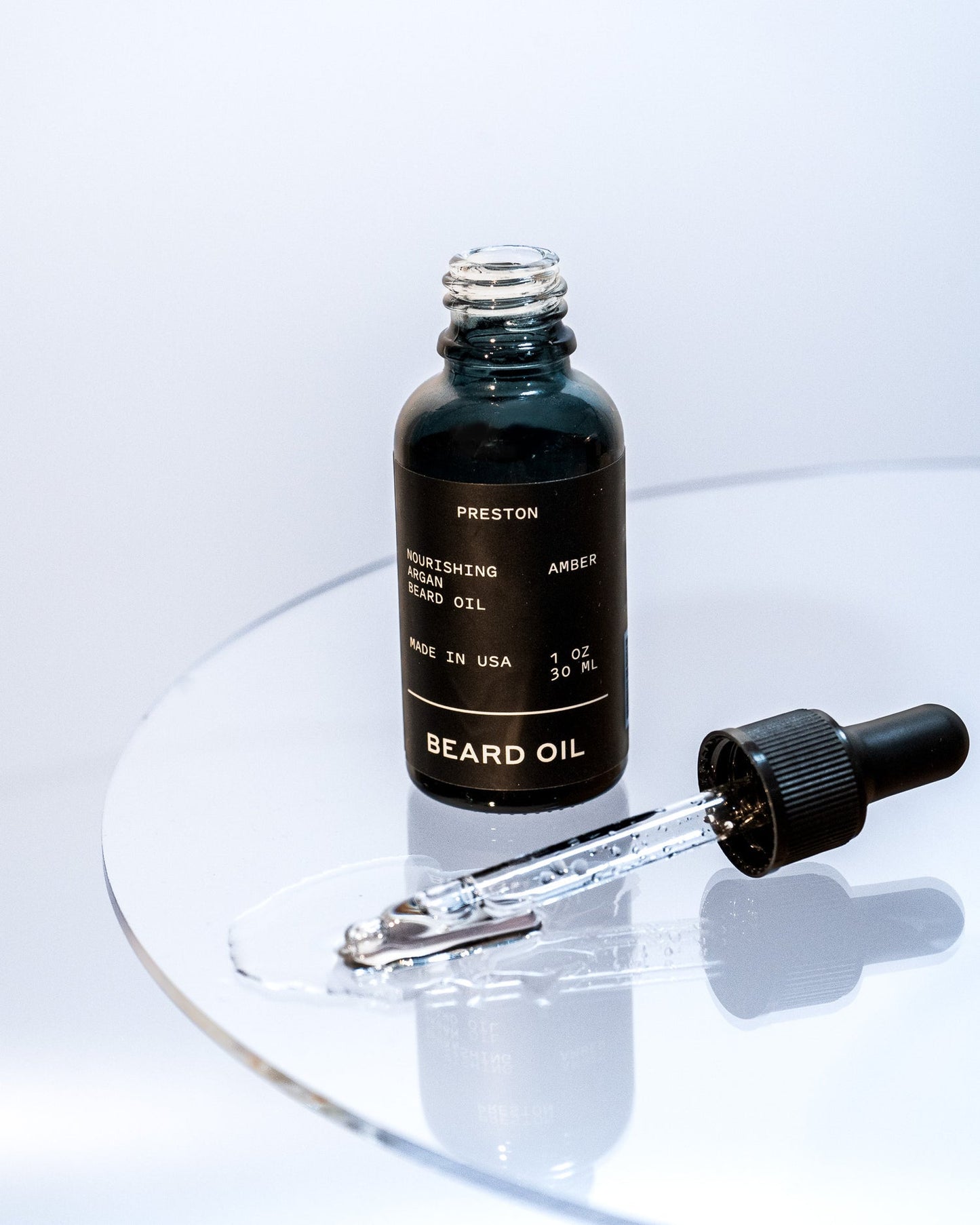 Amber beard oil bottle with dropper releasing oil onto surface