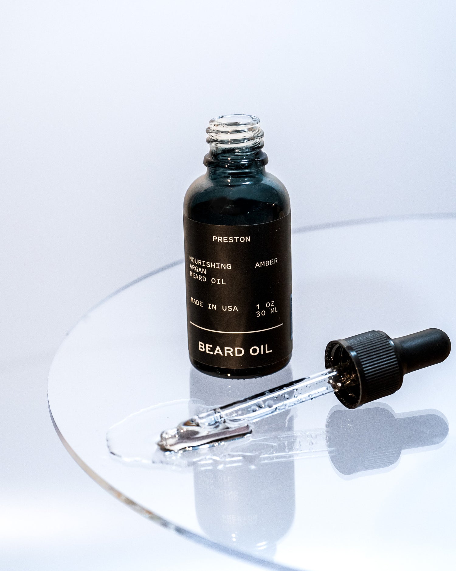 Amber beard oil bottle with dropper releasing oil onto surface