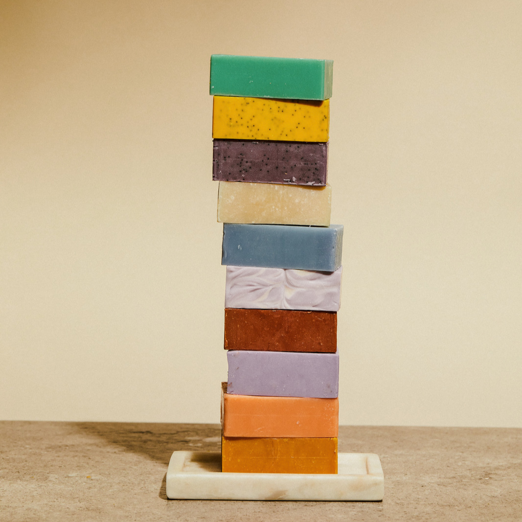 Tower of stacked bar soaps in green, yellow, purple, cream, and blue shades.