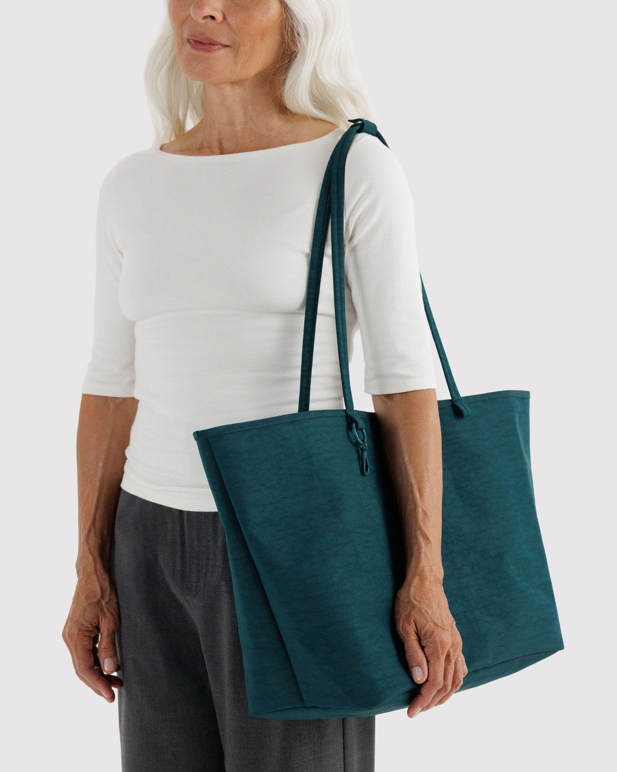 Large nylon reversible tote in deep teal with top handles on a person’s shoulder