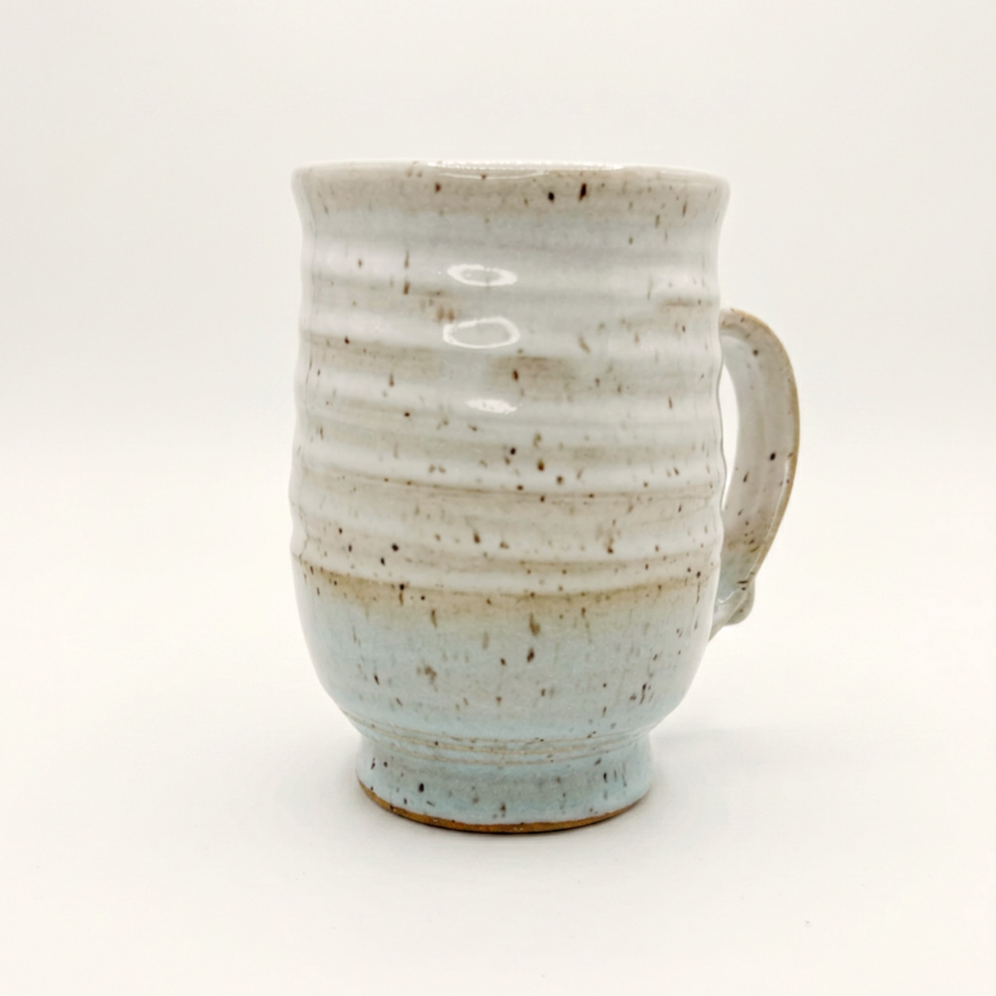 Speckled ceramic mug with curved handle, white top and blue-tinted bottom