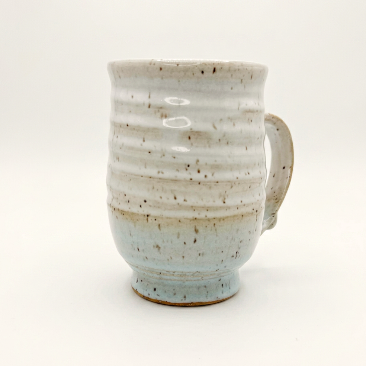 Speckled ceramic mug with curved handle, white top and blue-tinted bottom