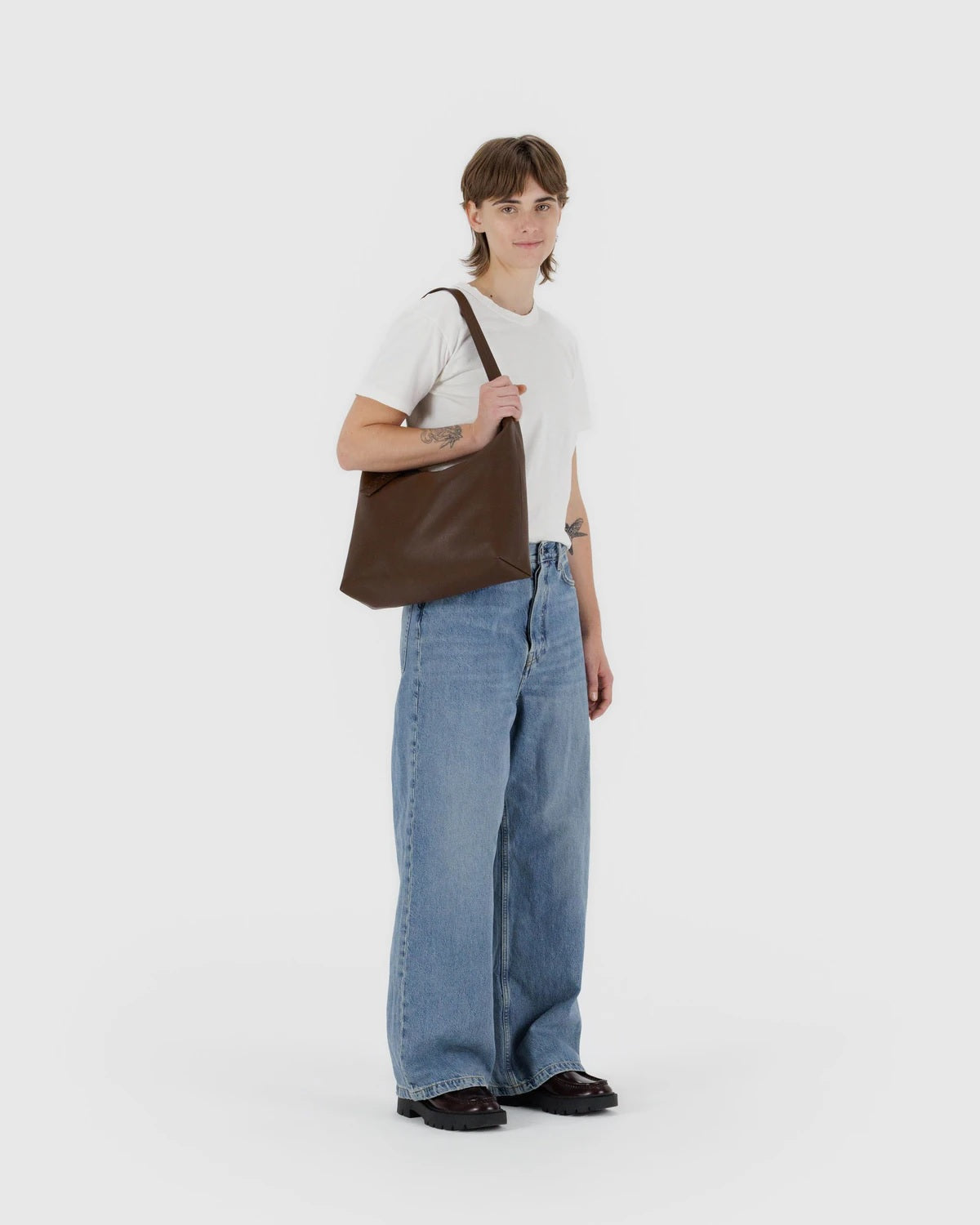Brown recycled leather shoulder bag with top handle and hanging charm, worn on model