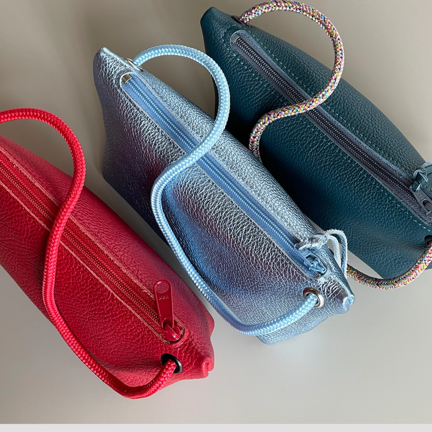 Two cord pouches, red and dark teal, with braided handles and zip pockets.