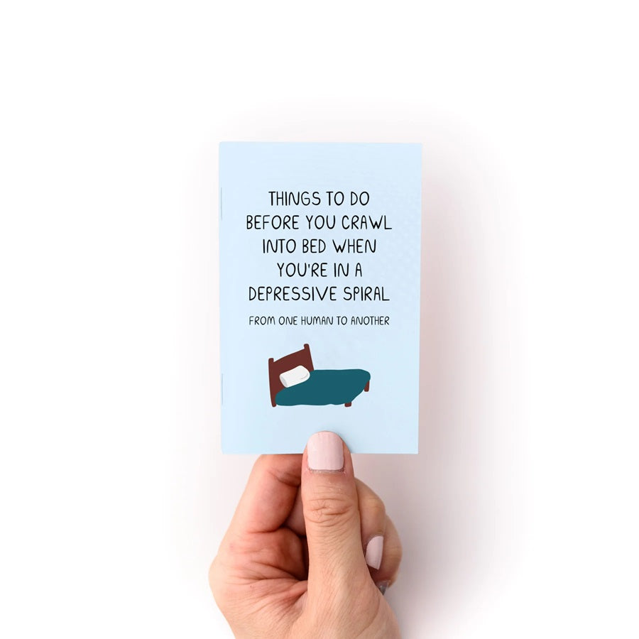 Zine booklet with teal front cover text about crawling into bed; illustrated bed icon