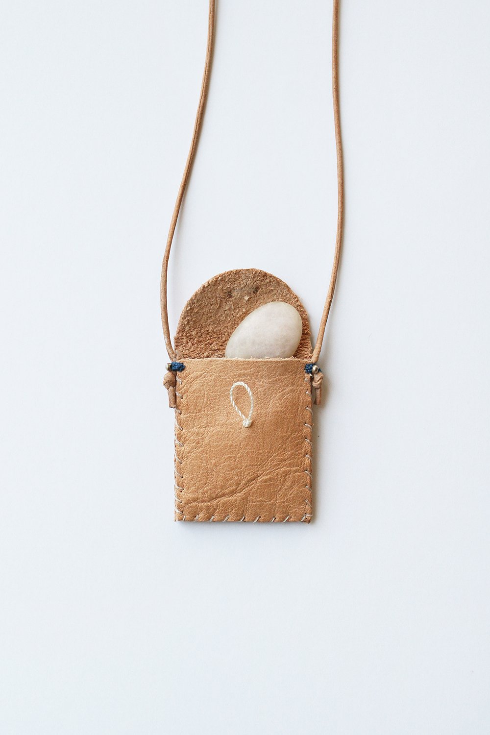 Tan leather amulet pouch with curved flap showing white stone inside