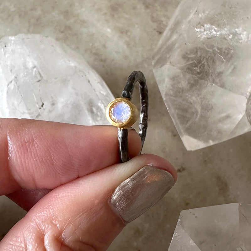 Moonstone ring featuring a round blue moonstone in a gold bezel on oxidized silver band
