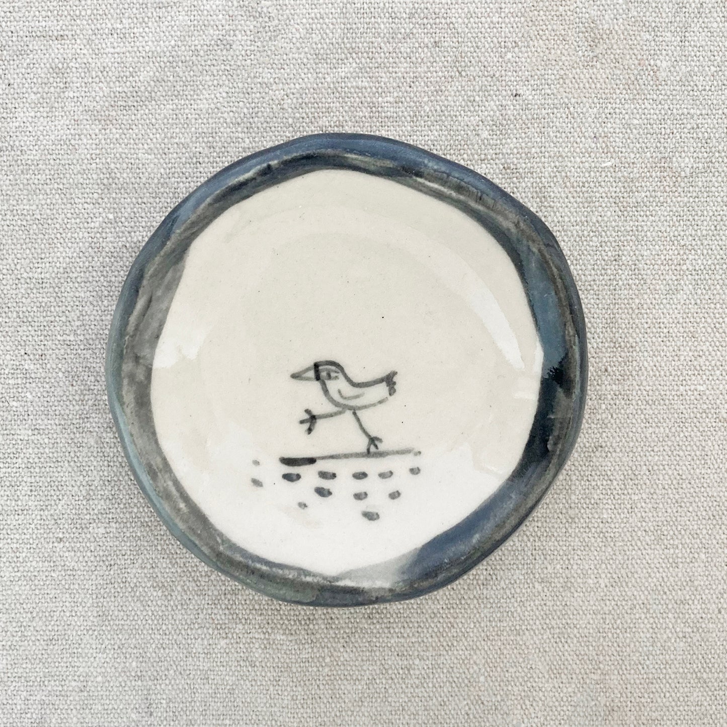 Handmade ceramic bird trinket dish, centered bird illustration with blue-glazed edge