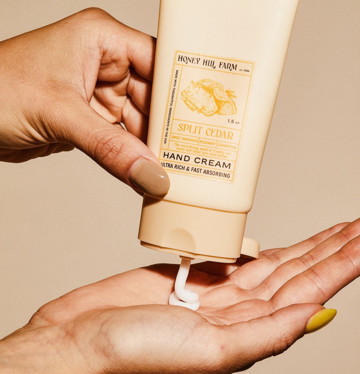 Hand cream tube dispensing white cream into open palm, Split Cedar scent