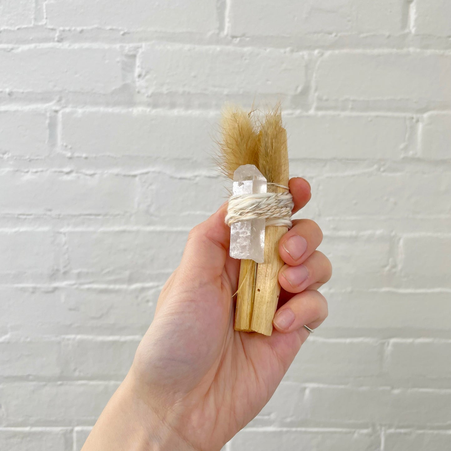 Handheld palo santo bundle with clear crystal point, wrapped with twine