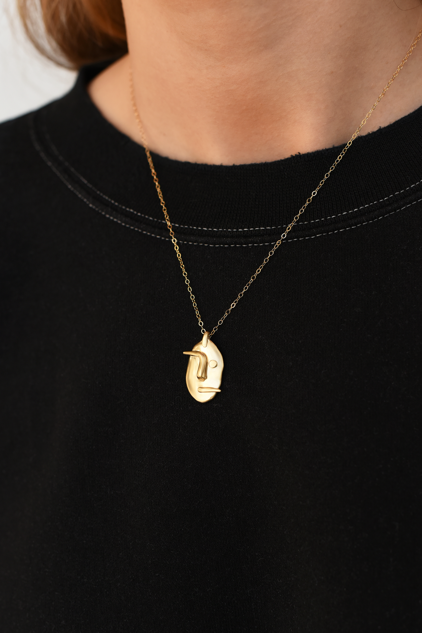 Brass face pendant necklace with face charm centered on gold-tone chain