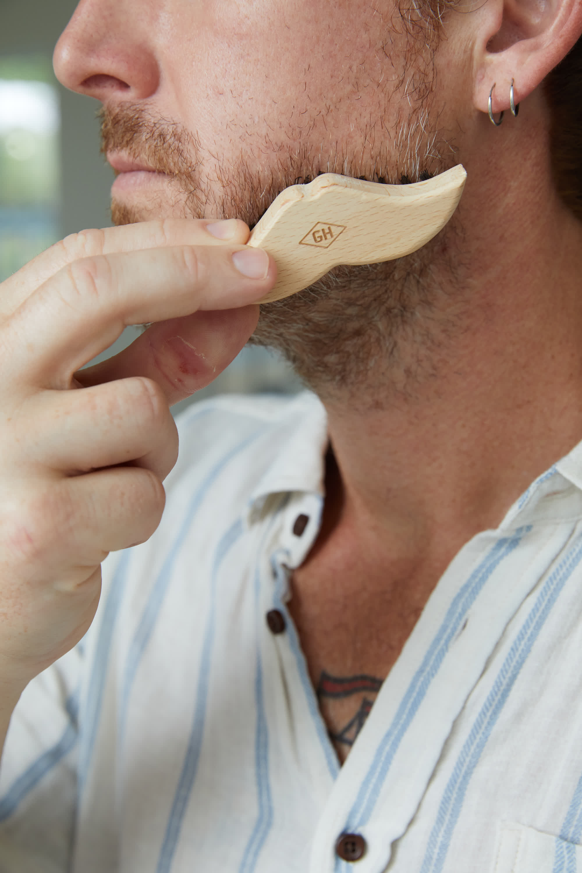 Wooden beard brush with pale handle and dense dark bristles, held near beard